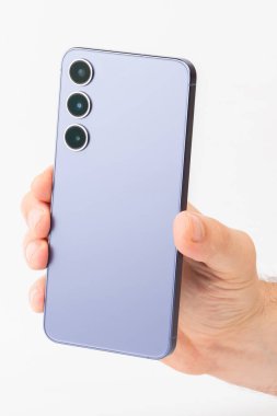 İyi ışıklandırılmış ortamda üç farklı kamera lensi bulunan şık bir akıllı telefon sahibi..