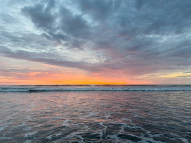 Güneş sakin okyanus sularının üzerinde batarken turuncu, pembe ve mor tonlarıyla boyanmış gökyüzü, barışçıl bir atmosfer yaratıyor..