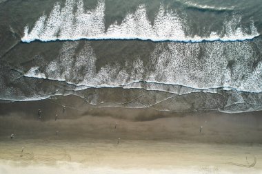 İnsanlarla dolu temiz bir sahil ve yüksek drone manzaralı uzun okyanus dalgaları.