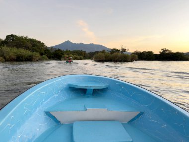 Gölde mavi tekne pruvası, günbatımında yanardağ.