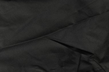 Dokulu siyah kumaş, yumuşak kıvrımlar ve yumuşak ışıklandırma altındaki gölgelerle karışık ayrıntılar gösterir..