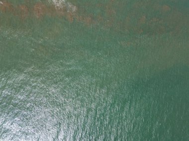 Okyanus dalgalarının kumlu plajla buluşmasını huzurlu bir şekilde izleriz. Huzurlu sahil bölgesinde güneş ışığı parıldar..