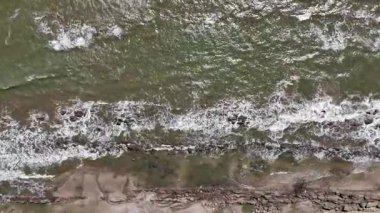 Dalgalar zarif bir şekilde kıyıya vurur ve alacakaranlıktaki sıcak ışığa karşı karmaşık desenler yaratır..