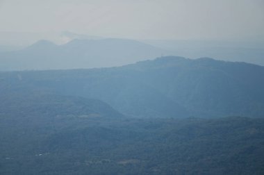 Dağların yumuşak mavi katmanları öğleden sonra güneşli bir gökyüzünün altında dingin bir manzara yaratır..