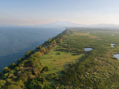 Sahil şeridi canlı yeşillik ve sakin sulara sahiptir, doğanın güzelliğini hava kararmadan hemen önce gösterir..