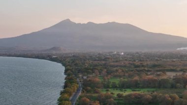 Gün batımında muhteşem göl manzarasının tadını çıkarın. Arka planda dağlar ve kıyı boyunca uzanan canlı ağaçlar..
