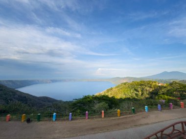 Nefes kesici manzara gösterileri sakin göl ile çevrili yemyeşil tepeler berrak mavi gökyüzü altında.