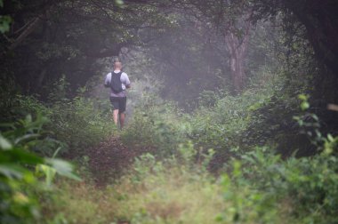 Sabahın erken saatlerinde sislerin altında sık ormanlarda insan dar bir yolda yürür..
