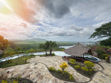 Sonsuz havuzu olan yemyeşil arazi günbatımı saatlerinde tropik tatil köylerindeki dağlara bakıyor..