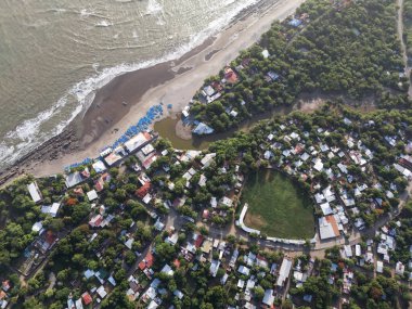 Hava manzarası kıyı kenarında canlı bir kasaba, gün ışığında evler, ağaçlar ve kumlu plaj alanları gösteriyor..