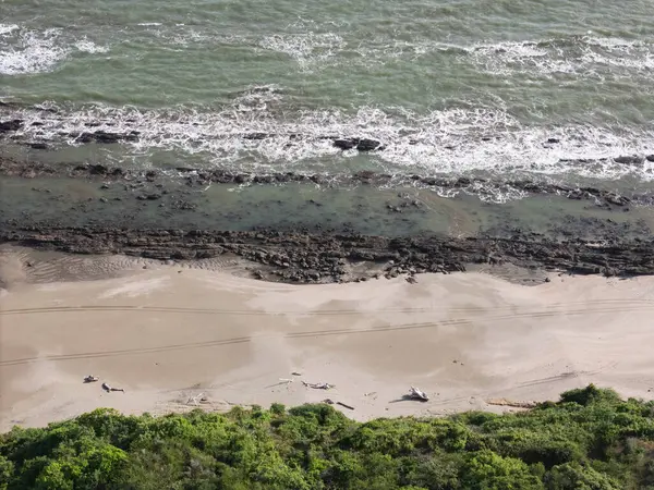 Kumlu sahil açık gökyüzünün altında uzanırken yumuşak dalgalar kayalara çarpıyor..