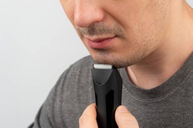 Adam parlak bir odada otururken sakalını elektrikli makasla kesmeye odaklanıyor..