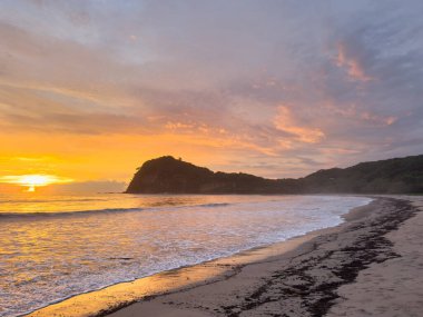 Alacakaranlıkta, turuncu günbatımı ışığında, okyanus kıyısı koyunda.