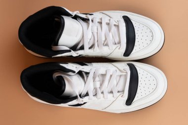 Siyah detaylara sahip modaya uygun beyaz spor ayakkabılar pürüzsüz ışık yüzeyinde oturur ve tasarımlarını gözler önüne serer..