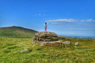 Kocaman bir granit kayanın üzerinde duran mutlu bir genç kız. Devon 'da Dartmoor yakınlarında çekilmiş.. 