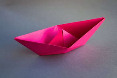 Pembe kağıt tekne origamisi boş gri bir arkaplanda izole edilmiş..