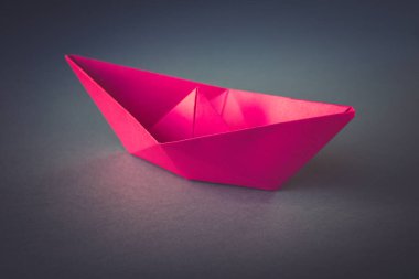 Pembe kağıt tekne origamisi boş gri bir arkaplanda izole edilmiş..
