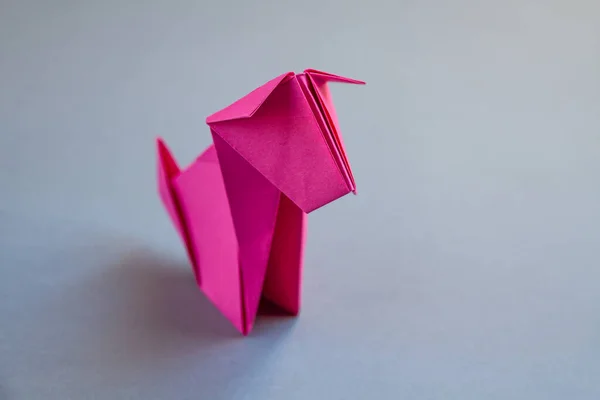 Pink paper dog origami isolated on a blank grey background.