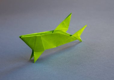 Yeşil kağıt köpek balığı origamisi gri bir arkaplanda izole edilmiş.