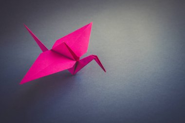 Pembe kağıt turna origamisi boş gri bir arkaplanda izole edilmiş..