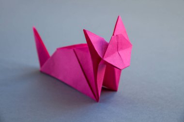 Pembe kağıt kedi origamisi boş gri bir arkaplanda izole edilmiş..