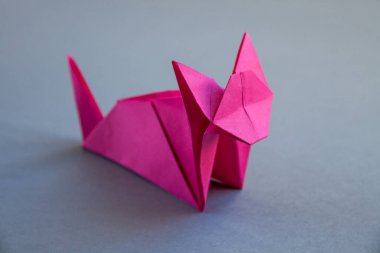 Pink paper cat origami isolated on a blank grey background.