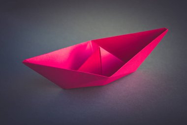 Pembe kağıt tekne origamisi boş gri bir arkaplanda izole edilmiş..