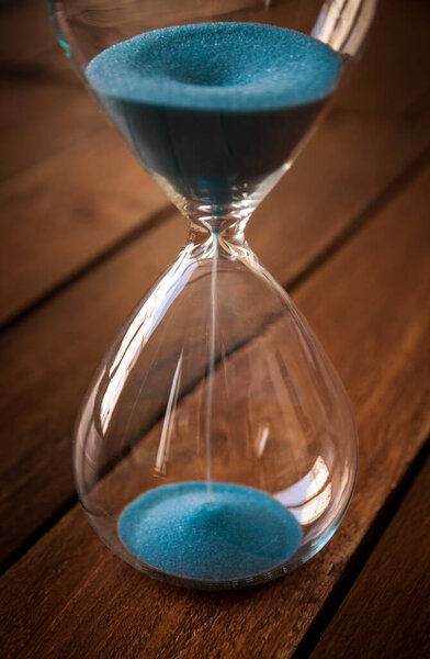 Hourglass containing blue sand on a rustic wooden board background