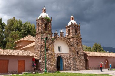Volkanik taştan yapılmış Raqchi Kilisesi dramatik bulutlu bir gökyüzüne karşı duruyor. Peru 'nun Cusco bölgesinde yer alan bina, Andean sömürge mimarisi ve tarihsel önemini yansıtıyor.