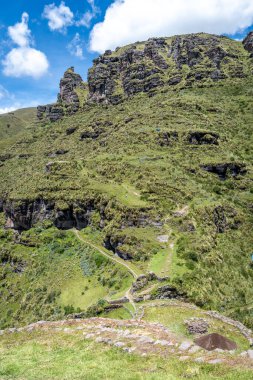 Waqrapukara 'nın antik taş duvarları ve terasları çevreleyen yeşil dağlarla harmanlanarak, İnka mühendisliğini bu uzak And arazisinde parlak bir gökyüzünün altında vurguluyor.