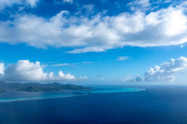 Fransız Polinezyası 'ndaki Tahaa adası, yukarıdan bakıldığında turkuaz bir göl, mercan resifi ve yemyeşil dağları ortaya çıkarır. Canlı okyanus renkleri koyu mavi Pasifik ile tezat oluşturuyor.