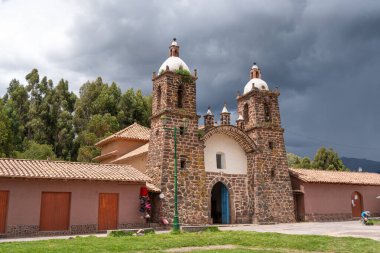 Volkanik taştan yapılmış Raqchi Kilisesi dramatik bulutlu bir gökyüzüne karşı duruyor. Peru 'nun Cusco bölgesinde yer alan bina, Andean sömürge mimarisi ve tarihsel önemini yansıtıyor.