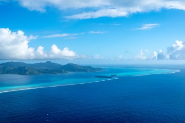 Fransız Polinezyası 'ndaki Tahaa adası, yukarıdan bakıldığında turkuaz bir göl, mercan resifi ve yemyeşil dağları ortaya çıkarır. Canlı okyanus renkleri koyu mavi Pasifik ile tezat oluşturuyor.