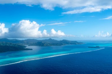 Fransız Polinezyası 'ndaki Tahaa adası, yukarıdan bakıldığında turkuaz bir göl, mercan resifi ve yemyeşil dağları ortaya çıkarır. Canlı okyanus renkleri koyu mavi Pasifik ile tezat oluşturuyor.