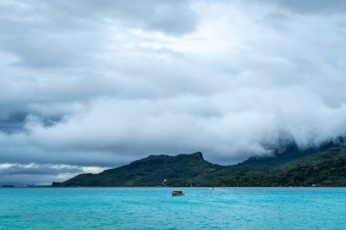 Bereketli dağları, berrak suları ve uzaktaki dramatik bulutlarıyla Bora Bora Adası 'nın çarpıcı panoramik manzarası.