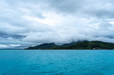 Bereketli dağları, berrak suları ve uzaktaki dramatik bulutlarıyla Bora Bora Adası 'nın çarpıcı panoramik manzarası.