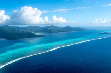 Fransız Polinezyası 'ndaki Tahaa adası, yukarıdan bakıldığında turkuaz bir göl, mercan resifi ve yemyeşil dağları ortaya çıkarır. Canlı okyanus renkleri koyu mavi Pasifik ile tezat oluşturuyor.