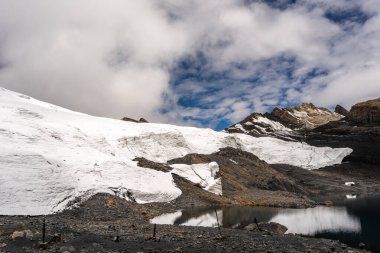 Huaraz, Peru 'da çarpıcı bir yüksek irtifa buz oluşumu olan Pastoruri Buzulu küçük bir buzul gölüne yansıyor. Bu geri çekilen buzullar, iklim değişikliğinin And arazisi üzerindeki etkilerini vurguluyor ve bölgede önemli bir yürüyüş noktası haline geliyor.