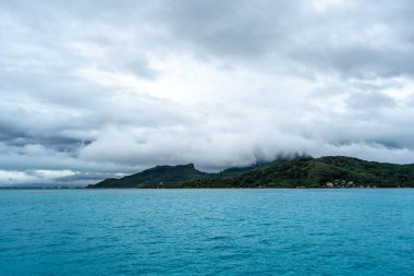 Bereketli dağları, berrak suları ve uzaktaki dramatik bulutlarıyla Bora Bora Adası 'nın çarpıcı panoramik manzarası.