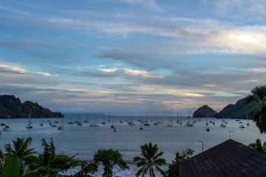 Nuku Hiva, Marquesas Adaları 'ndaki Taiohae Körfezi' nin üzerindeki gökyüzü, bereketli dağların yakınında yelkenlilerin demirlediği sakin okyanusu yansıtan ılık günbatımı renkleriyle parıldıyor. Fransız Polinezyası