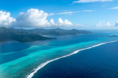 Fransız Polinezyası 'ndaki Tahaa adası, yukarıdan bakıldığında turkuaz bir göl, mercan resifi ve yemyeşil dağları ortaya çıkarır. Canlı okyanus renkleri koyu mavi Pasifik ile tezat oluşturuyor.