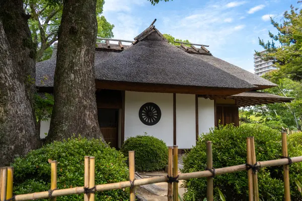 Japonya 'nın Hiroşima kentindeki sakin Shukkei-en Japon bahçesinde manikürlü yeşilliklerle çevrili geleneksel sazdan bir kulübe.