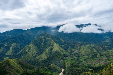Sulawesi, Endonezya 'daki Toraja bölgesi boyunca yemyeşil dağlar, bulutlu bir gökyüzünün altında sisli tepelere tutunarak uzanır.