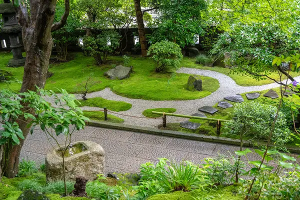 Japonya 'nın Kamakura kentindeki Hokoku-ji tapınağındaki ağaçların ve yeşilliklerin arasında yosun kaplı bir toro feneri duruyor.