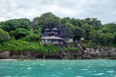 Endonezya 'nın Sulawesi kentindeki Bira Sahili' nin turkuaz sularının üzerindeki yeşil kayalıklara tutunan ahşap evler, verimli tropikal ormanlarla çevrilidir.