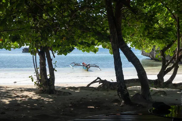 Geleneksel ahşap bir tekne, Lia sahilinin beyaz kumları yakınında, Waleakodi Adası, Togian takımadaları, Sulawesi, Endonezya 'da parlak mavi bir gökyüzünün altında yüzmektedir.