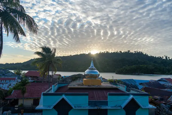 Pulau Papan camisi Endonezya 'nın Sulawesi kentindeki Malenge Adası üzerindeki sıcak günbatımı ışığında aydınlanan balıkçıların evleri arasında yer alıyor.