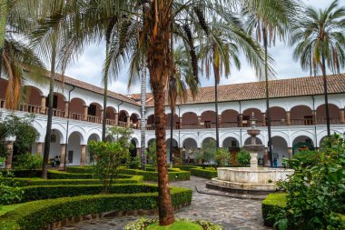 Quito, Ekvador 'daki tarihi San Francisco manastırı ve kilise avlusunda koloni mimarisi, palmiye ağaçları ve sakin bir çeşme yer alıyor.