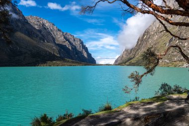 Çarpıcı bir turkuaz göl, yüksek dağların arasına kurulmuş mavi gökyüzünü yansıtır. Huzurlu manzara ünlü Laguna 69 Huaraz, Peru yürüyüşünün bir parçasıdır.