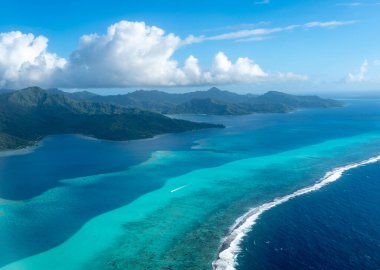 Fransız Polinezyası 'ndaki Tahaa adası, yukarıdan bakıldığında turkuaz bir göl, mercan resifi ve yemyeşil dağları ortaya çıkarır. Canlı okyanus renkleri koyu mavi Pasifik ile tezat oluşturuyor.